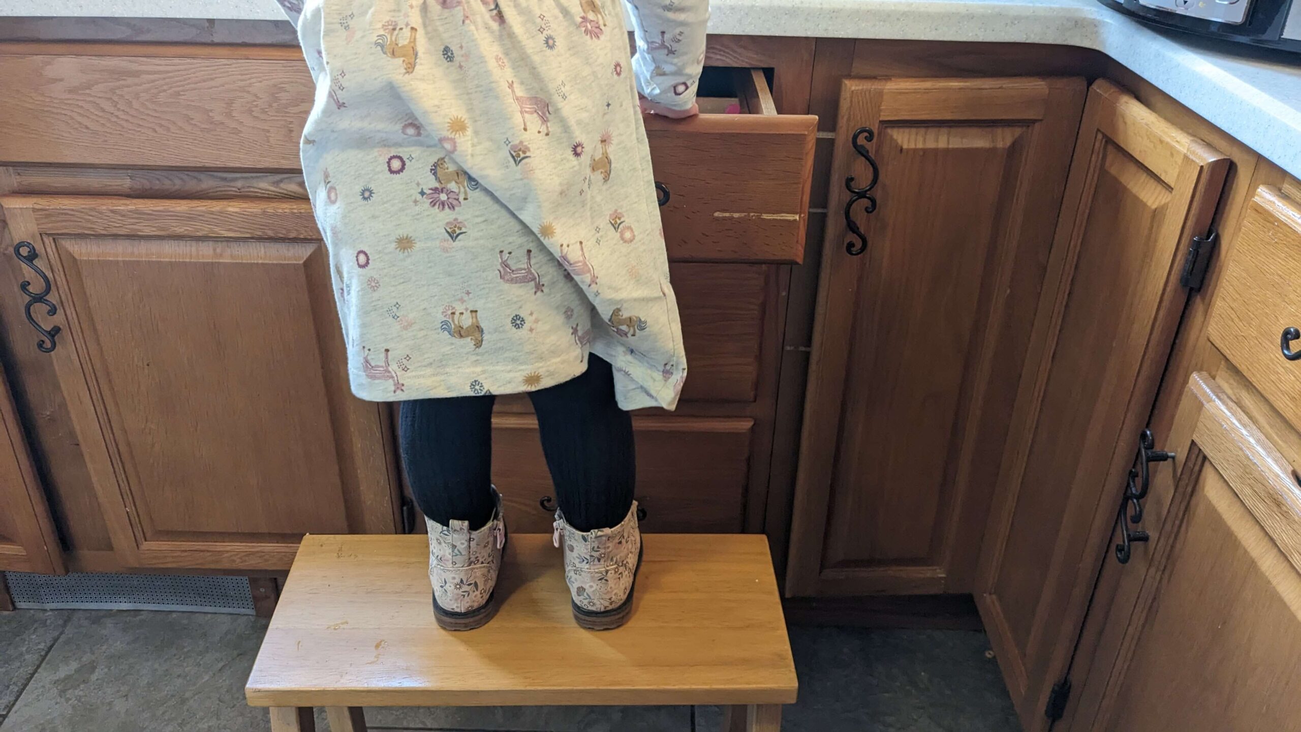 toddler standing on a step stool in front of a drawer