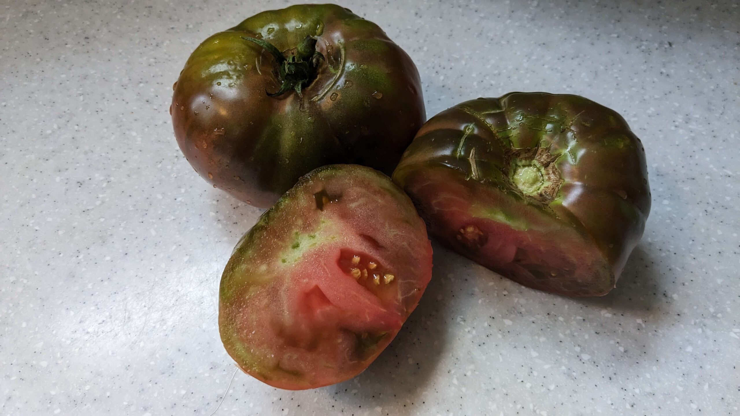 Two black beauty tomatoes, one sliced in half to show the pink a dark red insides