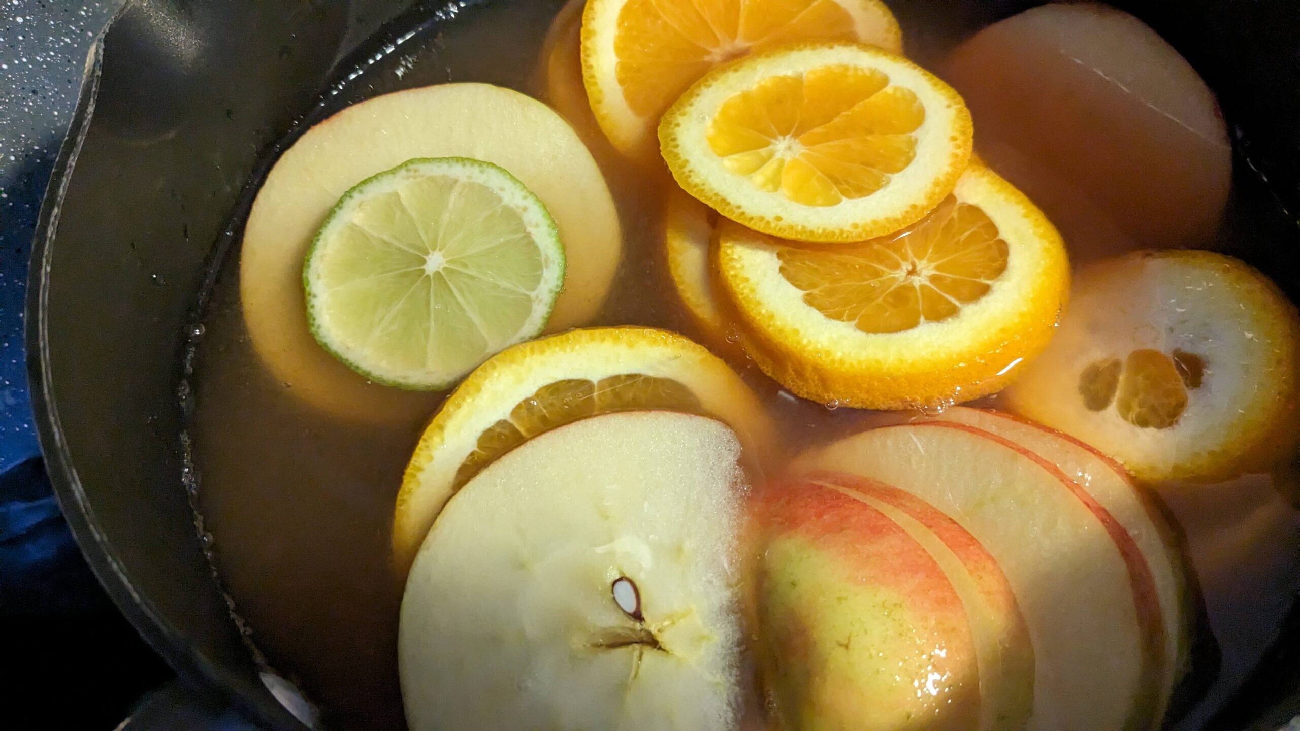 slices of oranges, limes, and apples in a pot of apple juice