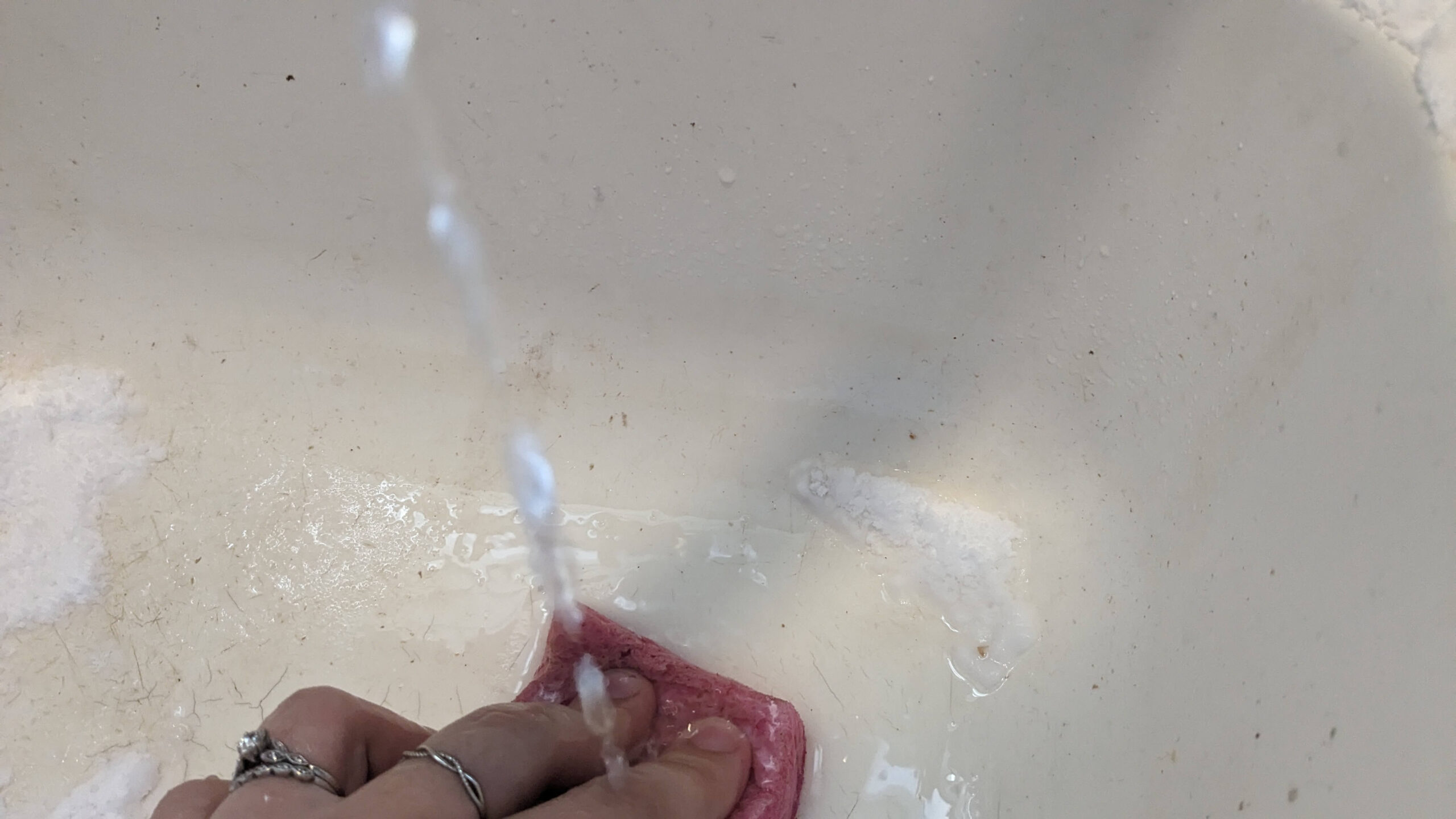 woman scrubbing a dirty sink with a sponge under running water