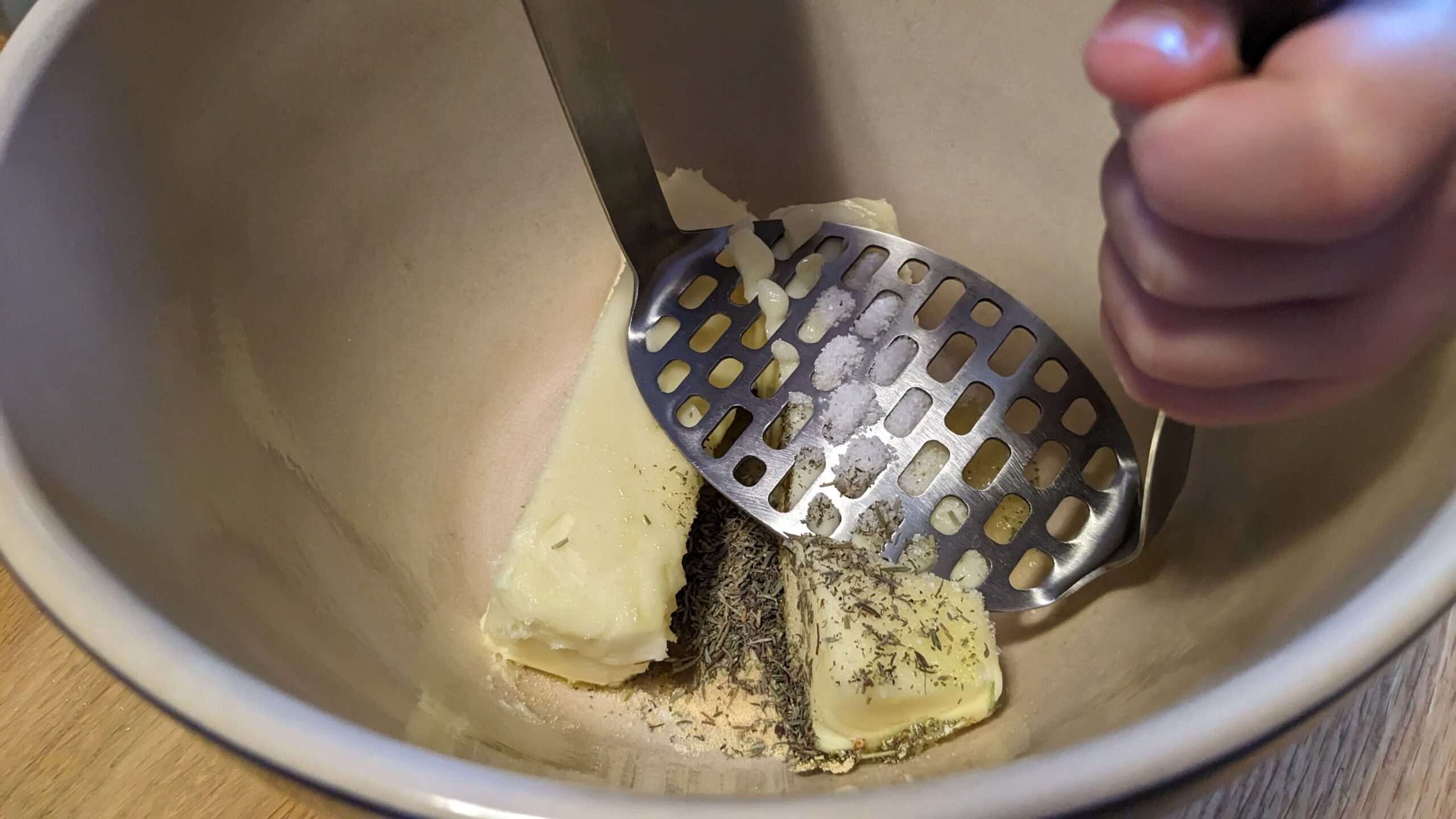 toddler mashing butter and herbs together in a bowl