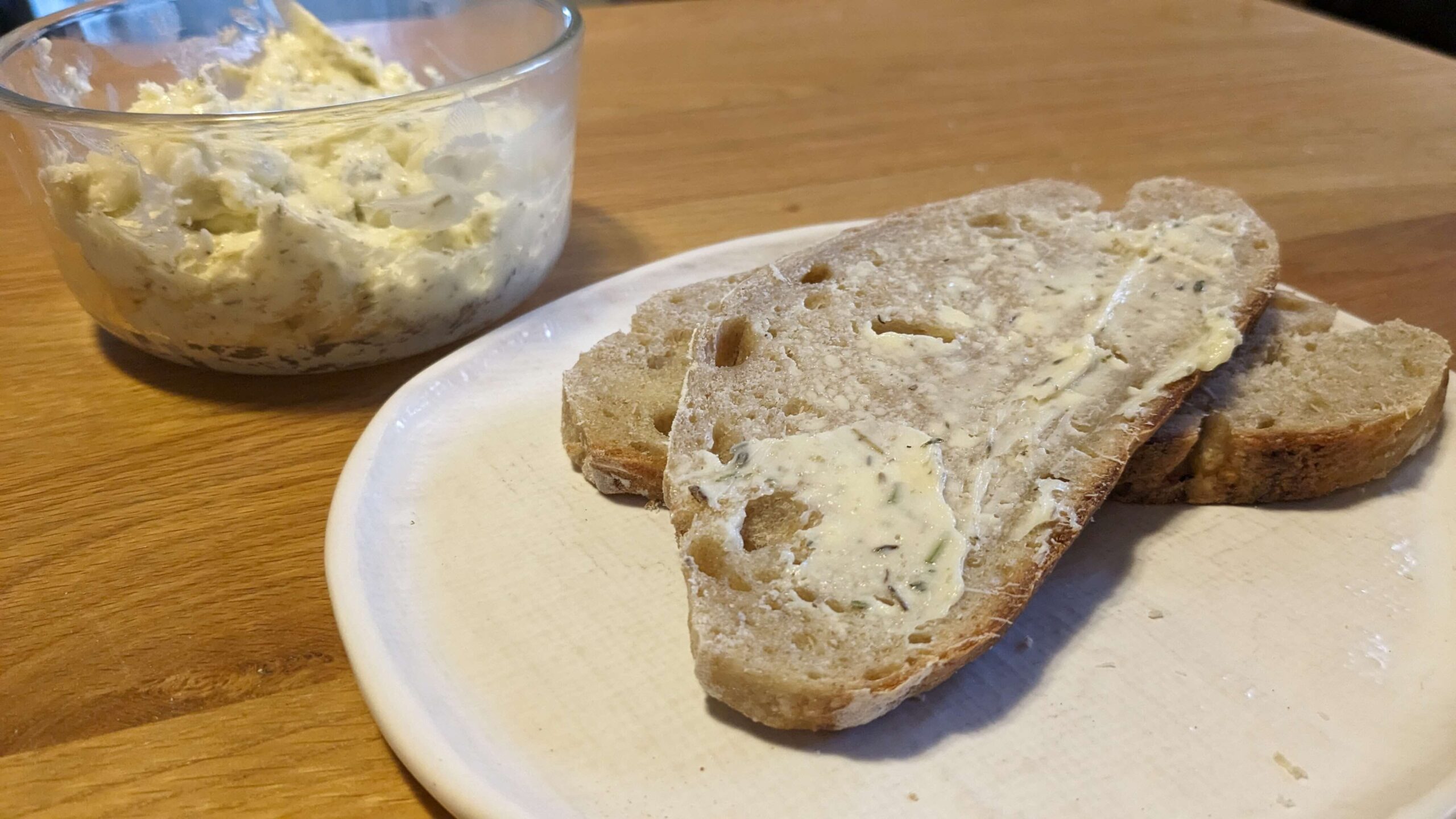 two slices of artisan toast, one buttered next to a bowl of compound herb butter