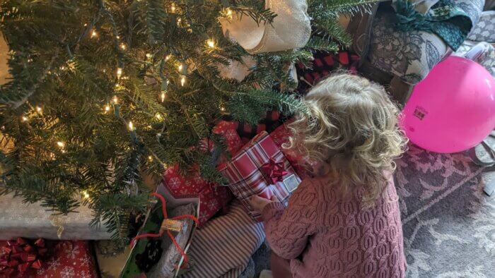 toddler girl placing a gift underneath the Christmas tree