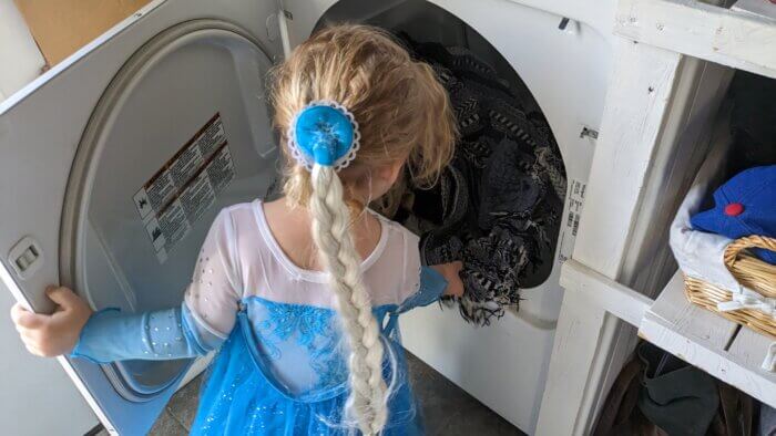 toddler girl dressed like Elsa putting laundry in the dryer