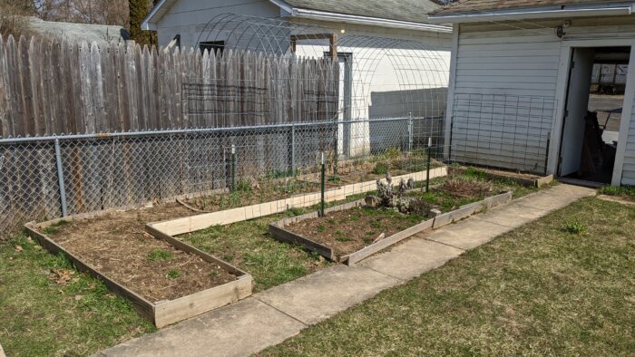 A small and large raised bed filled with soil in front of a fence.