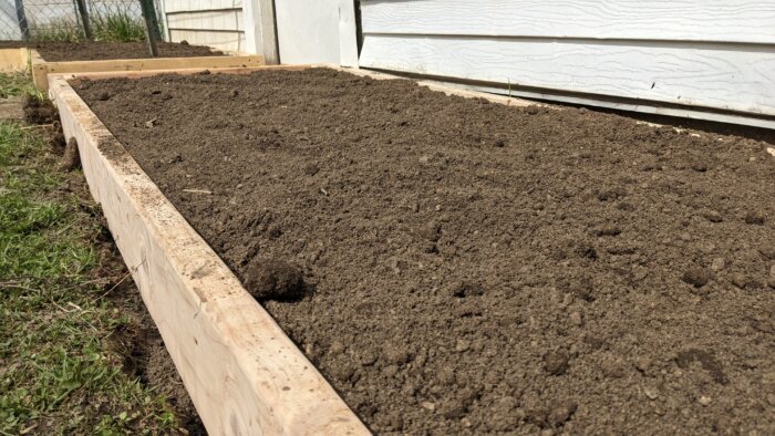 A flat surface of soil sitting inside of a raised bed.