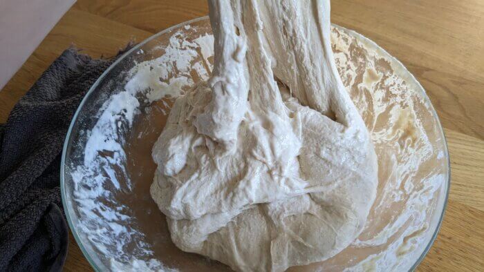 dough being stretched in a glass bowl