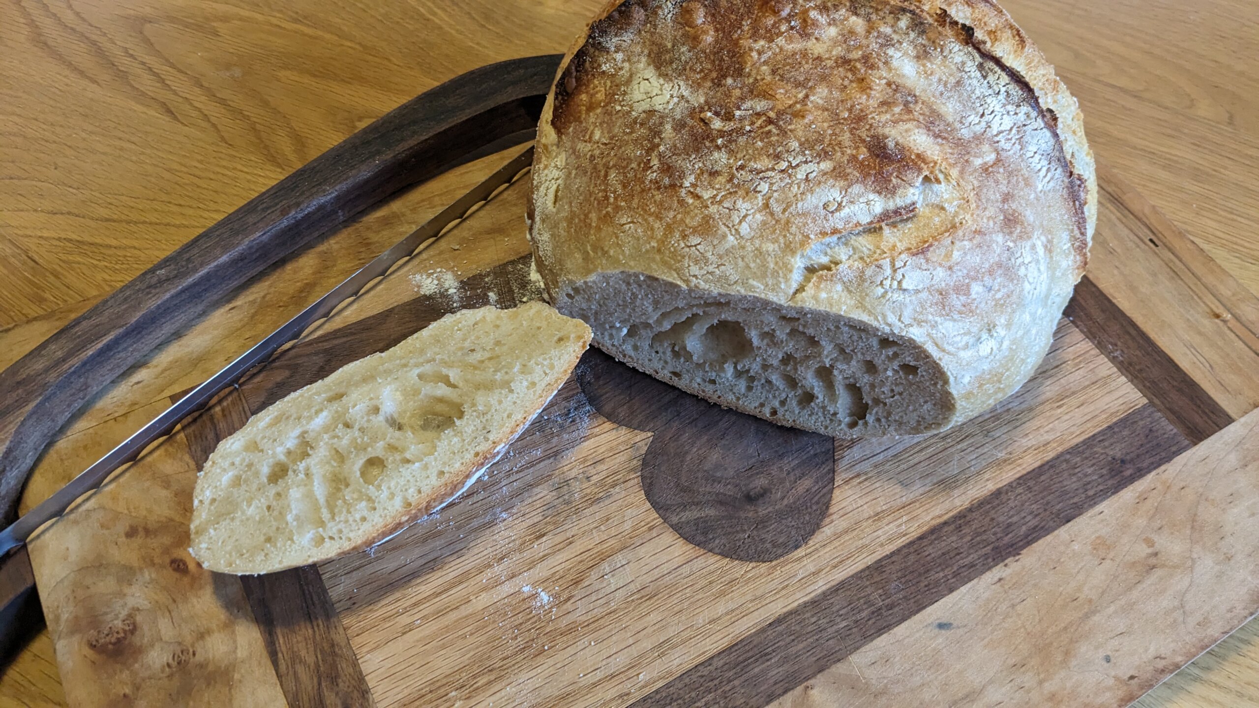 a sliced artisan sourdough loaf next to a bow knife on a cutting board 