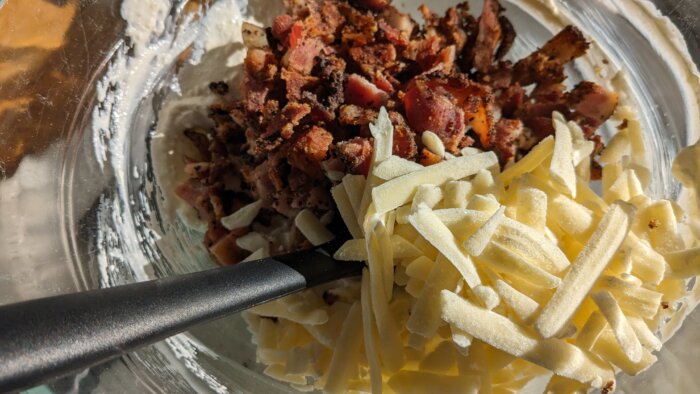 a bowl with cooked chopped bacon and shredded white cheddar cheese.