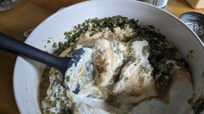 herbs partially incorporated into a bowl of greek yogurt and sour cream
