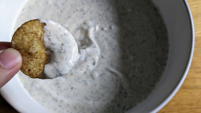 woman holding a chip with ranch dressing over a bowl of ranch dressing