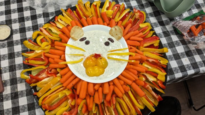a bowl of ranch dressing surrounded by cut carrots and colored bell peppers. 