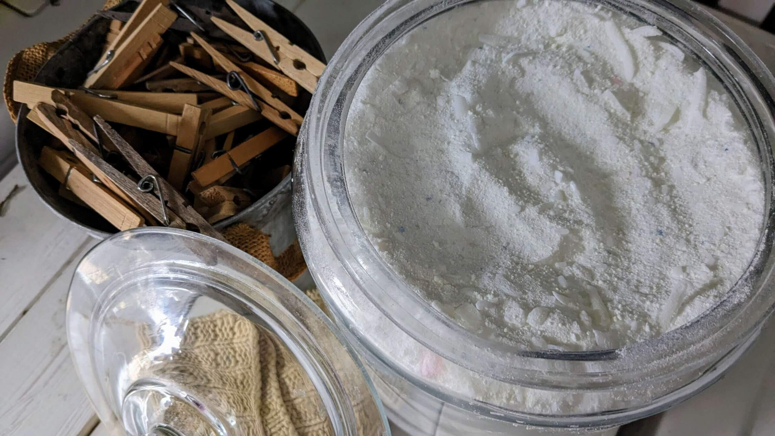 a bucket of clothespins next to a glass lid next to a jar of powdered laundry detergent