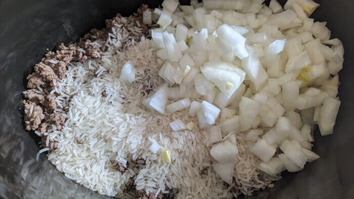 a crock pot with cooked ground beef, uncooked white rice, and raw diced onions