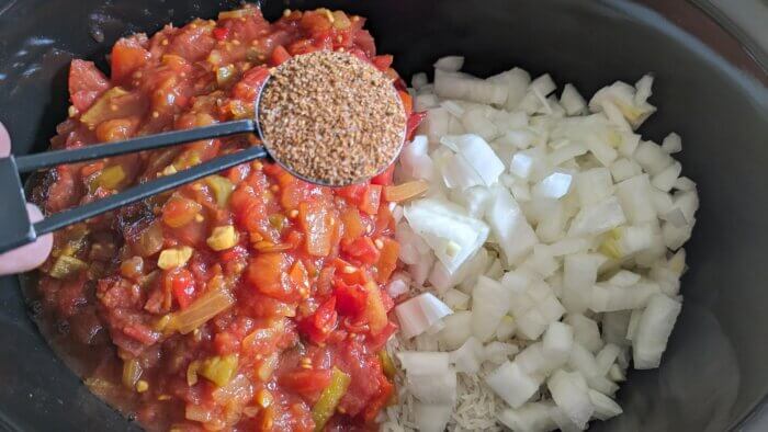 a crock-pot with diced tomatoes, diced, raw onions, and a tablespoon of brown spices