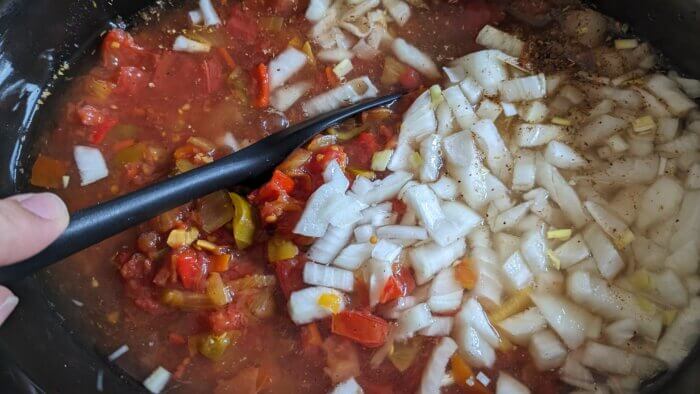 a crock pot of soup being stirred by a black spatula