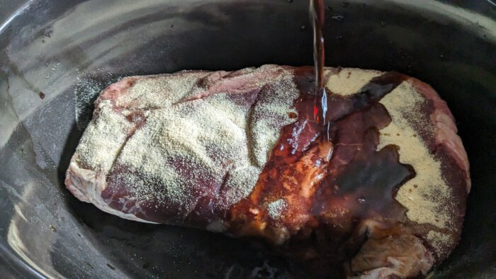 soy sauce pouring onto a roast covered in garlic powder in a crock pot