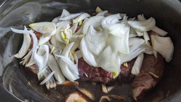sliced raw onions on a roast in a crock pot