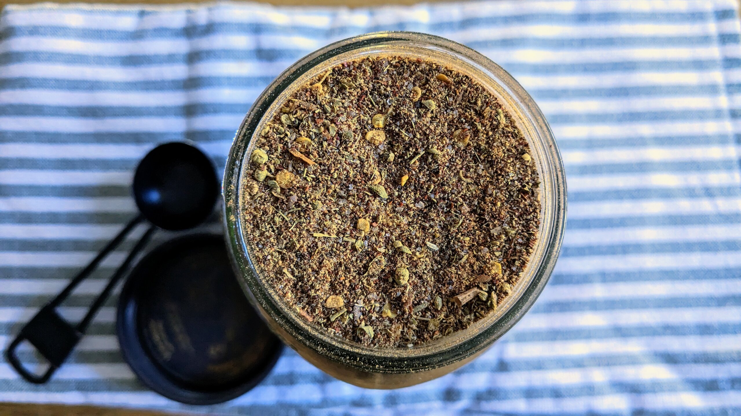 an overhead view of bulk homemade taco seasoning next to a mason jar lid and tablespoon on top of a green and white striped towel