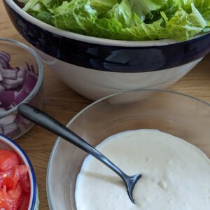 bowl of homemade caesar dressing in front of salad supplies