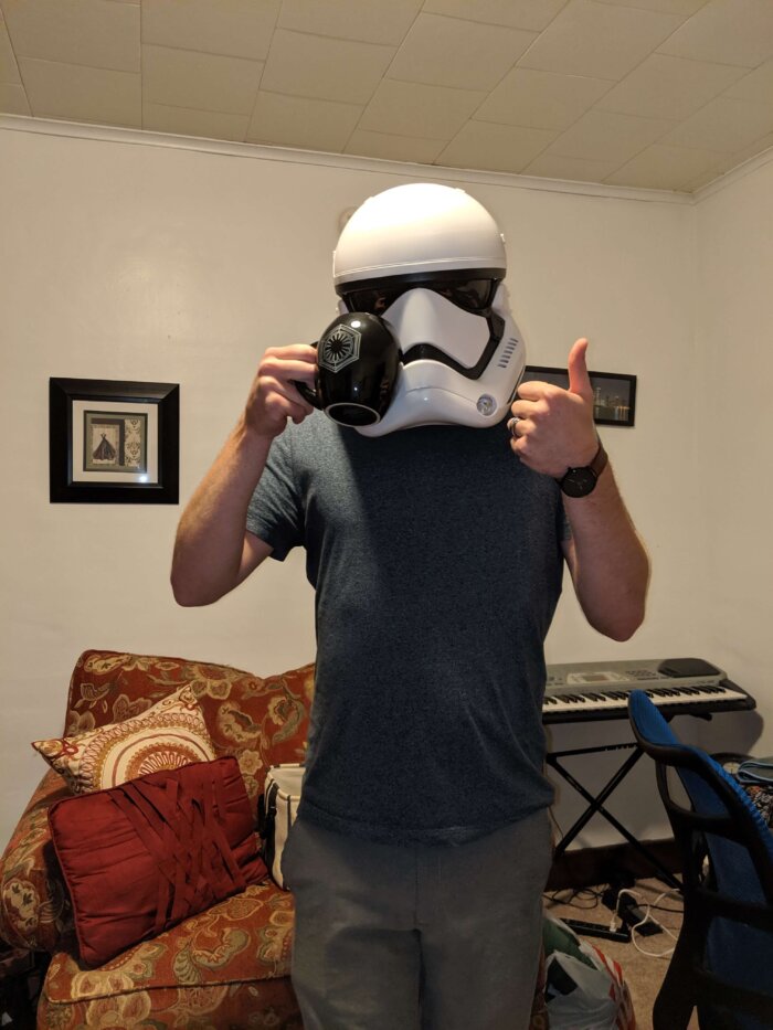 man wearing a storm trooper helmet and holding a coffee cup giving a thumbs up