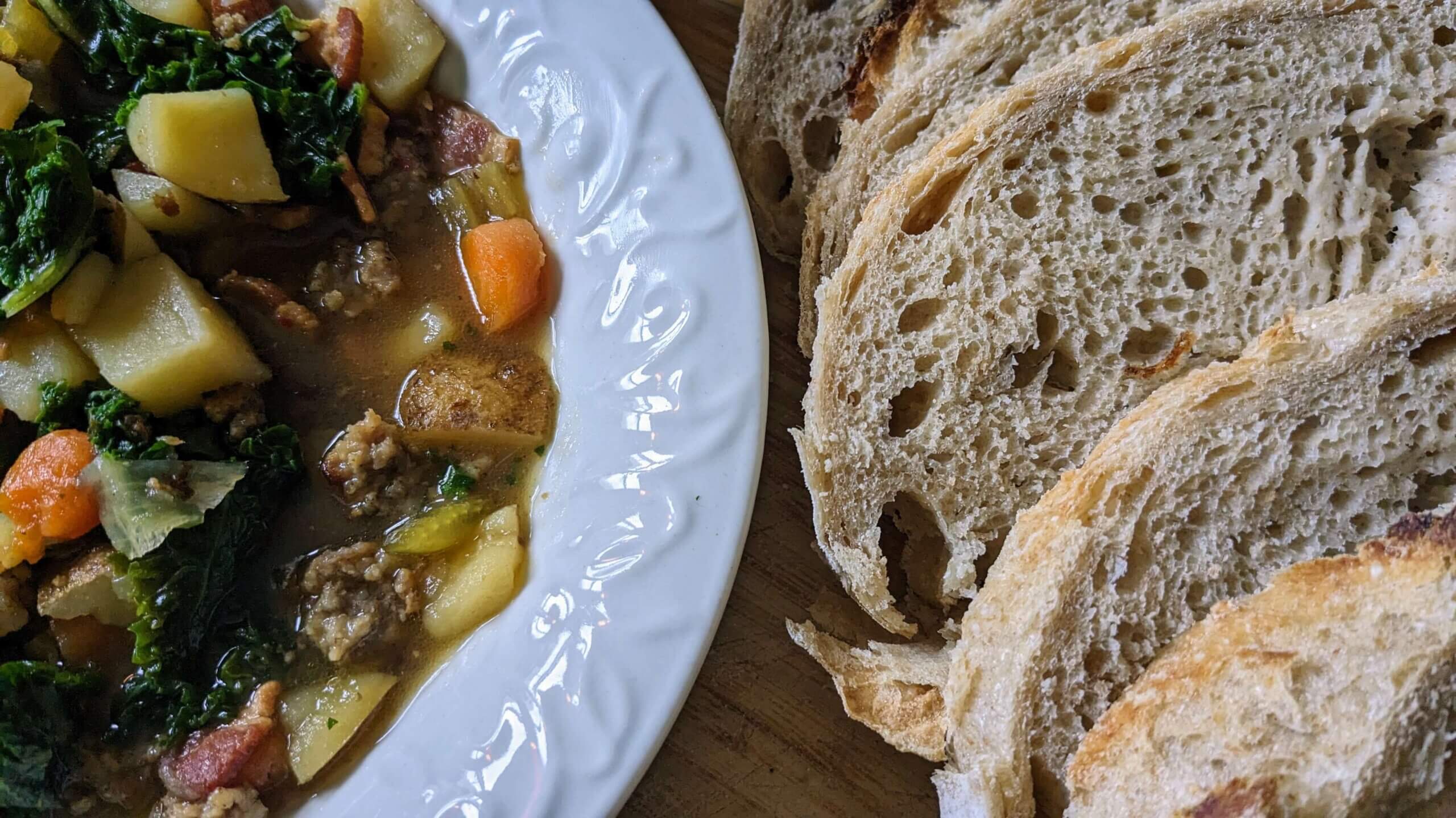 sausage, bacon and Kale soup in a bowl next to sliced artisan sourdough bread