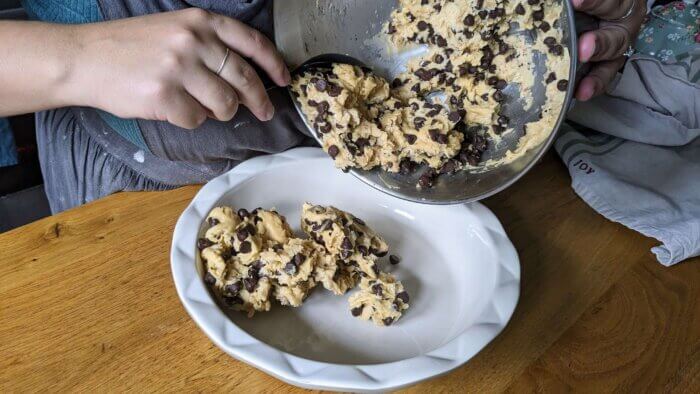 woman scooping raw sourdough chocolate chip cookie dough batter into a pie plate