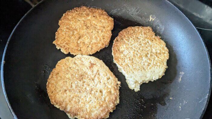 three oatmeal pancakes cooking in a skillet