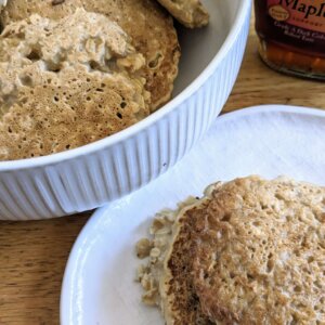 oatmeal pancakes in a bowl next to a plate of oatmeal pancakes