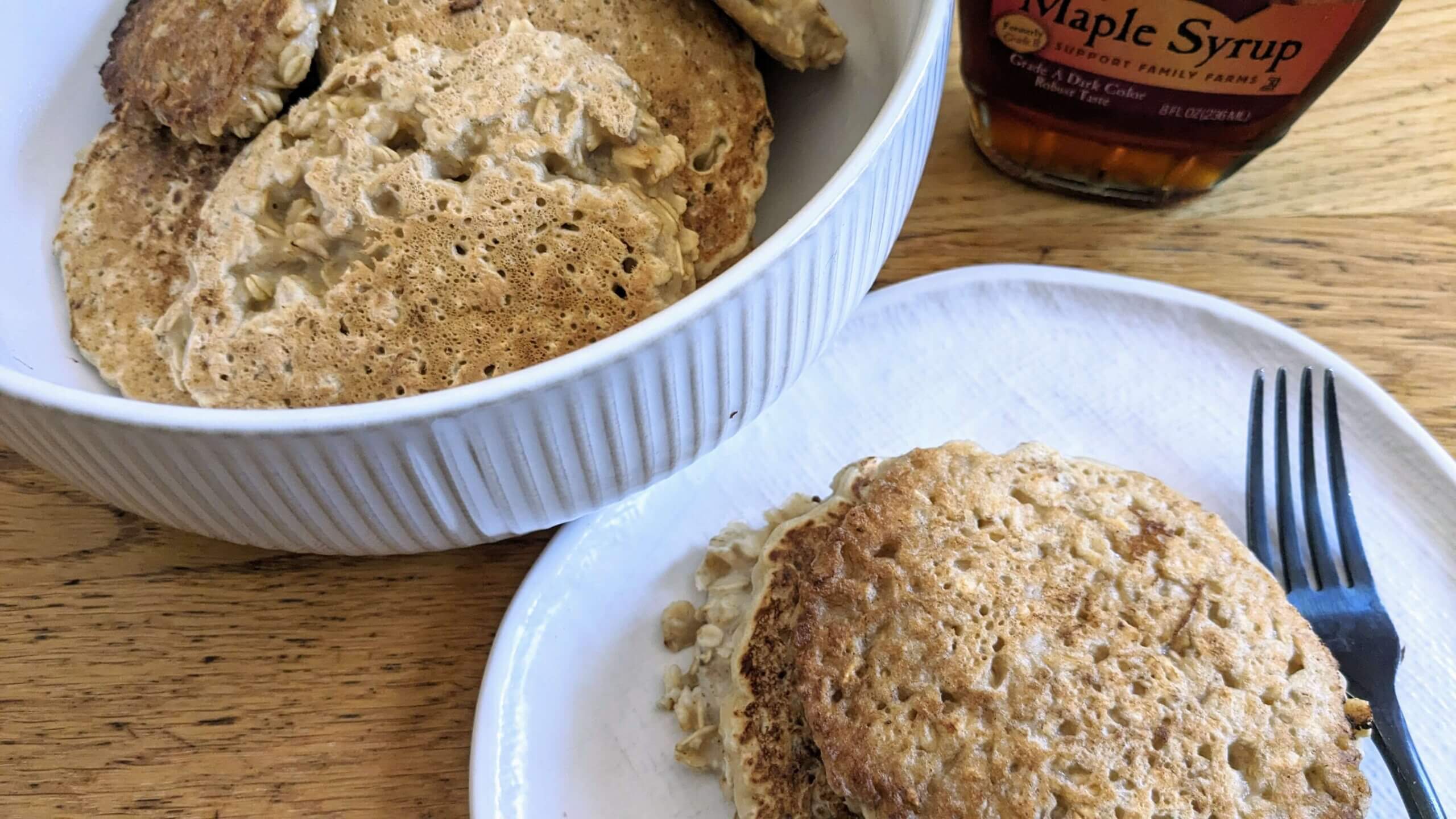 oatmeal pancakes in a bowl next to a plate of oatmeal pancakes