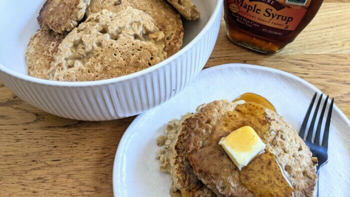 oatmeal pancakes in a bowl next to a plate of oatmeal pancakes topped with butter and syrup