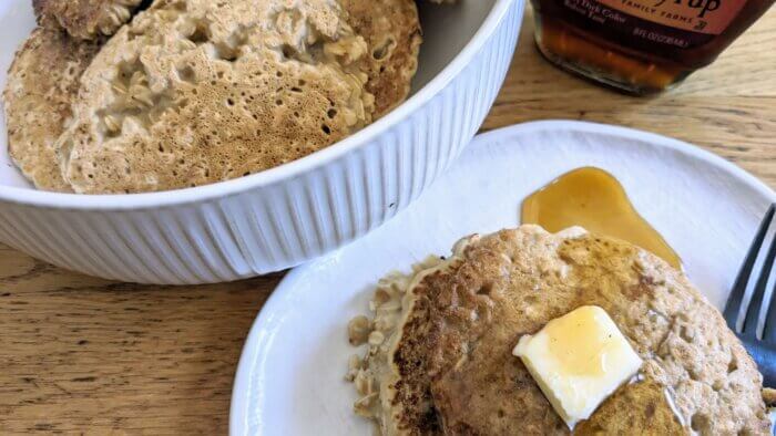 oatmeal pancakes in a bowl next to a plate of oatmeal pancakes topped with butter and syrup