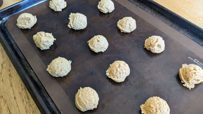 gluten free peanut butter cookie batter in balls on a sil pat on a cookie sheet