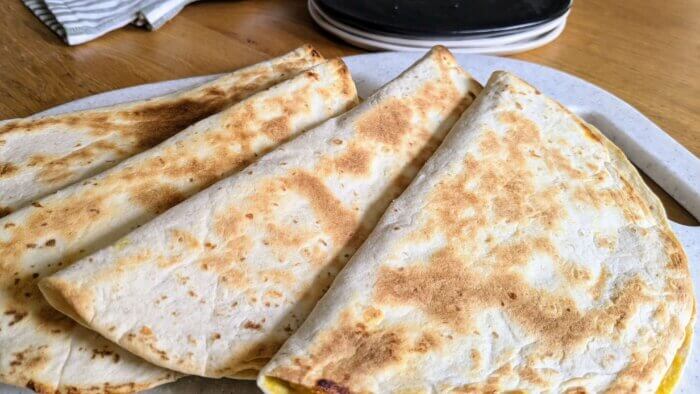 four half apple quesadillas on a white cutting board next to plates