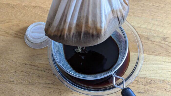 cold brew coffee concentrate filtering through cheesecloth over a fine mesh strainer