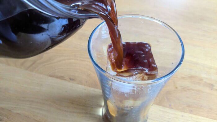 pouring cold brew coffee concentrate over a glass of ice