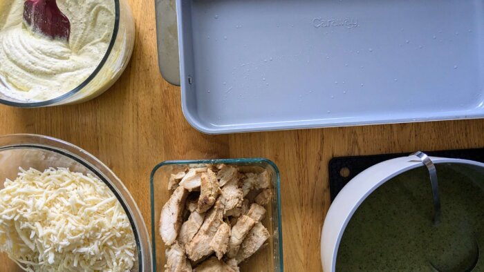 a 9x13 pan, a bowl of chicken, a bowl of mozzarella cheese, a bowl of pesto sauce, and a bowl with a ricotta cheese mixture