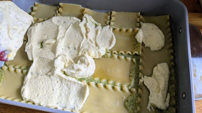 ricotta cheese mixture being spread over cooked lasagna noodles