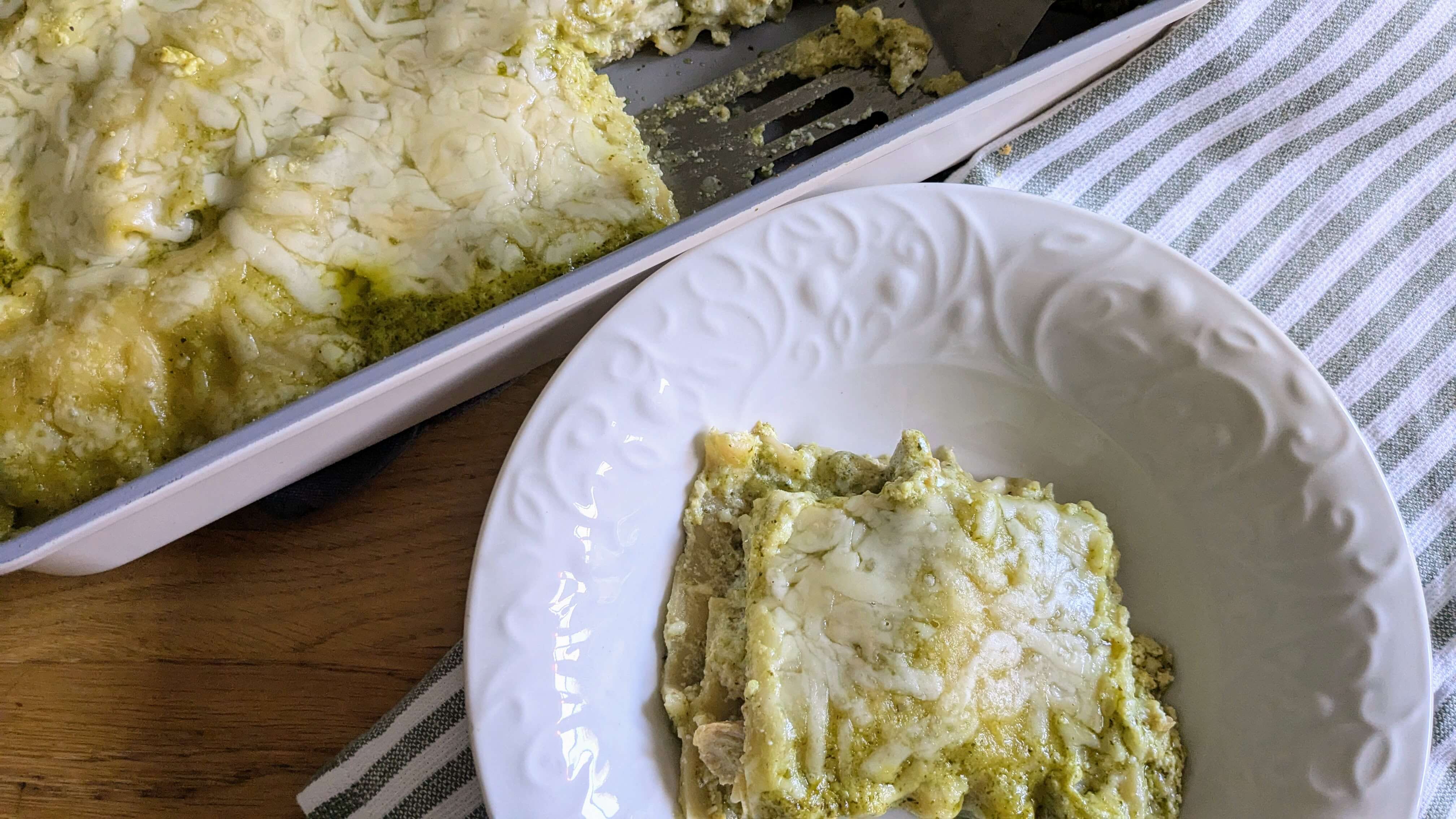 a white bowl with pesto chicken lasagna next to a pan of pesto chicken lasagna