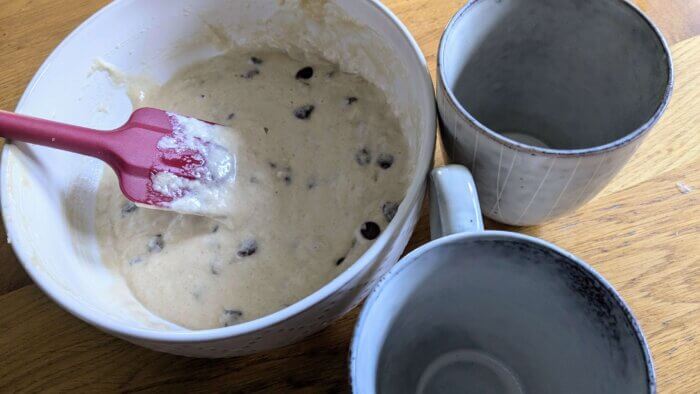 sourdough chocolate chip mug cake batter next to two empty mugs