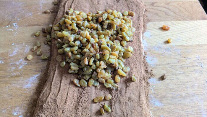 sourdough Cinnamon raisin bread dough on a counter rolled out into a long rectangle, topped with cinnamon and raisins