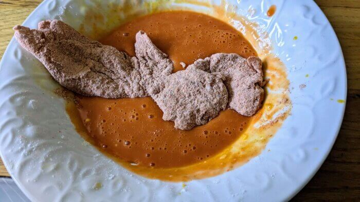 chicken dredged in flour and cayenne pepper being dredged in an egg and hot sauce mixture