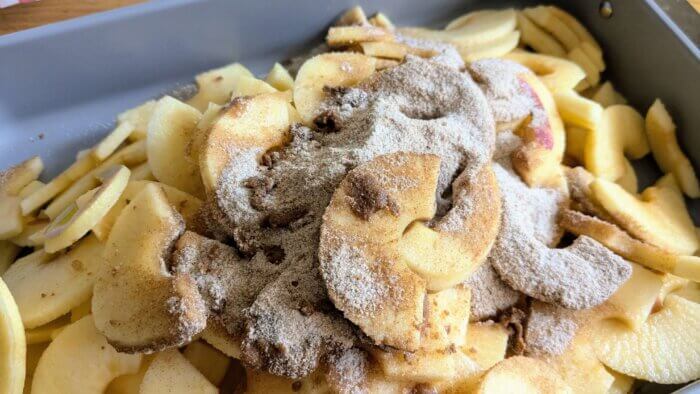 a pile of raw sliced apples topped with a cinnamon, flour, sugar mixture