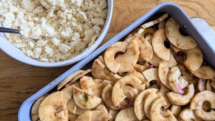 a bowl of raw crumb topping next to a pan of sliced apples