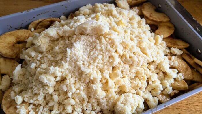 a raw crumb topping on top of a pan of sliced apples