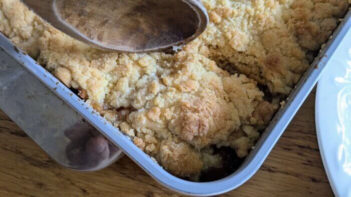 a wooden spoon scooping out baked apple cobbler