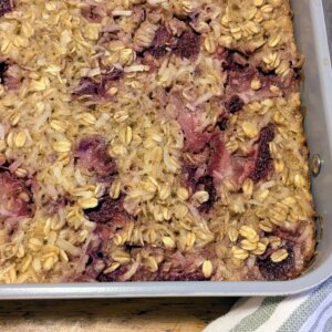 Strawberry coconut oatmeal bake in a 9x13 pan next to a wooden spoon on a towel