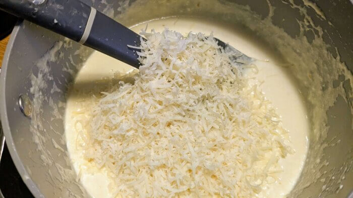 shredded parmesan cheese being stirred into a cream sauce