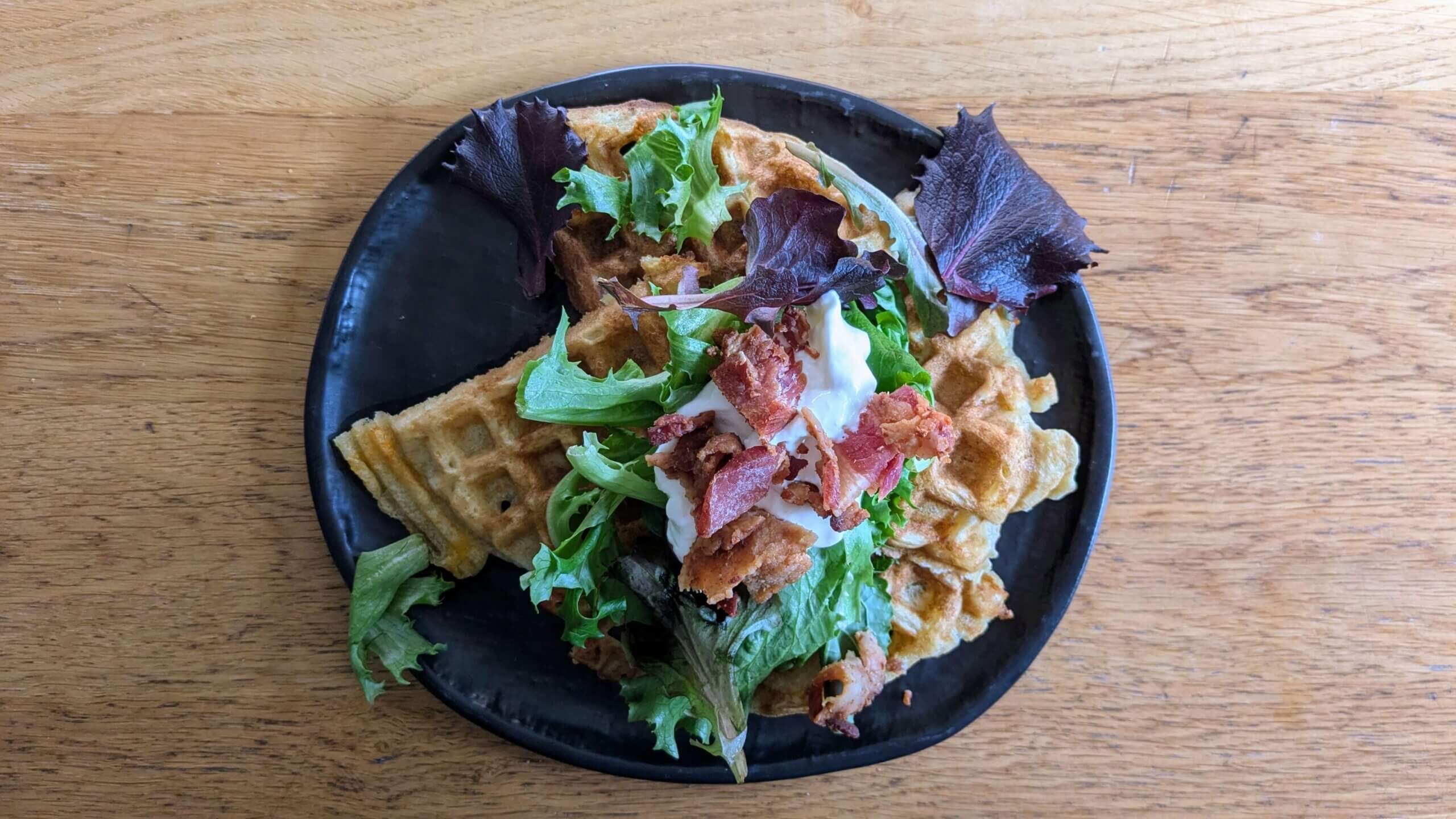 Cheddar Parmesan sourdough waffles topped with leafy greens, sour cream, and bacon.