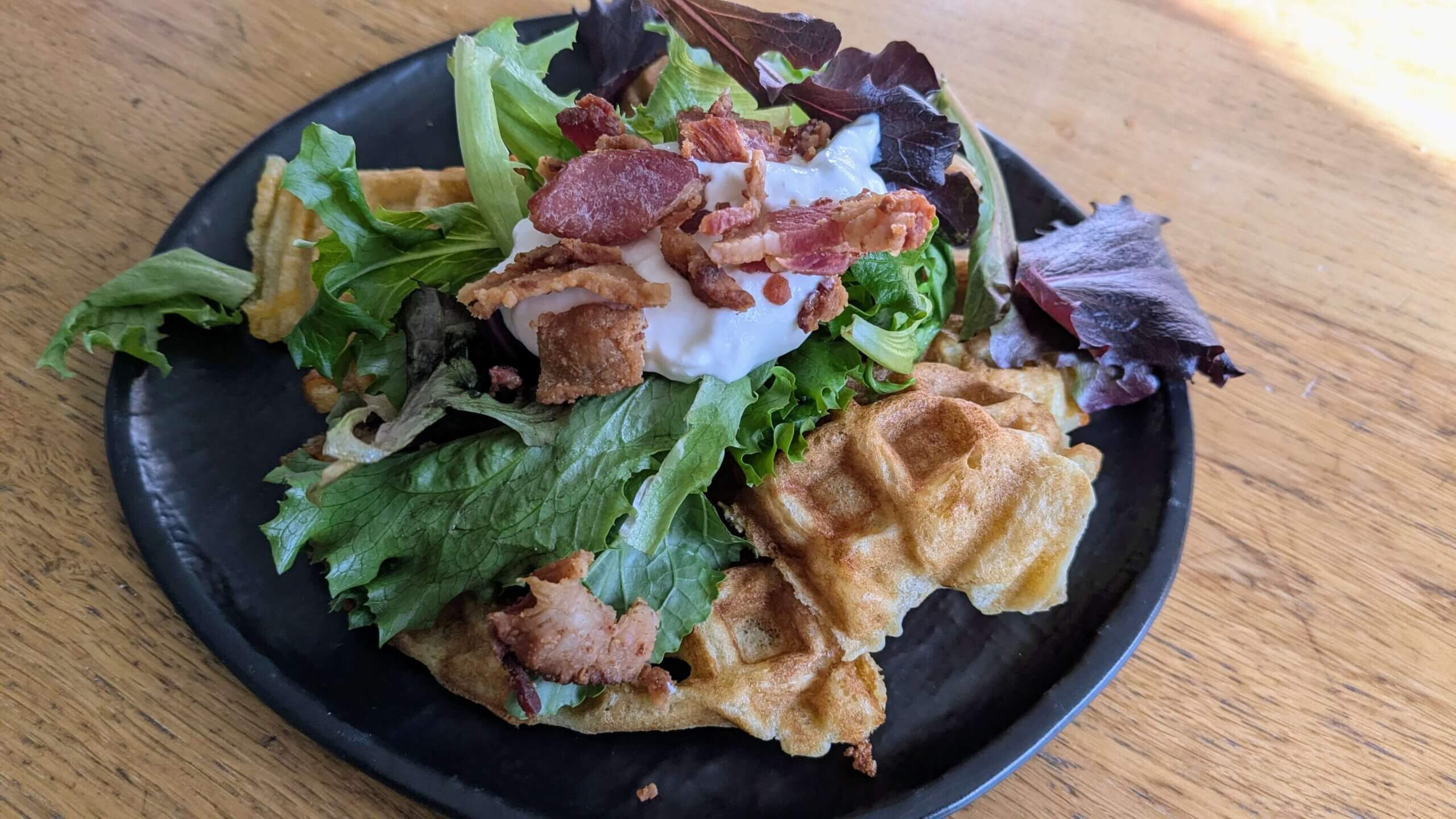 Cheddar Parmesan sourdough waffles topped with leafy greens, sour cream, and bacon.